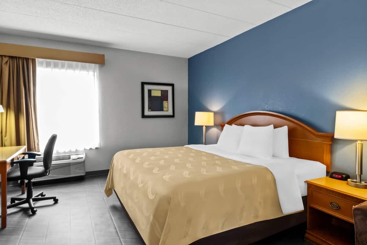 A hotel room with a bed, desk, chair, and a picture on the wall.