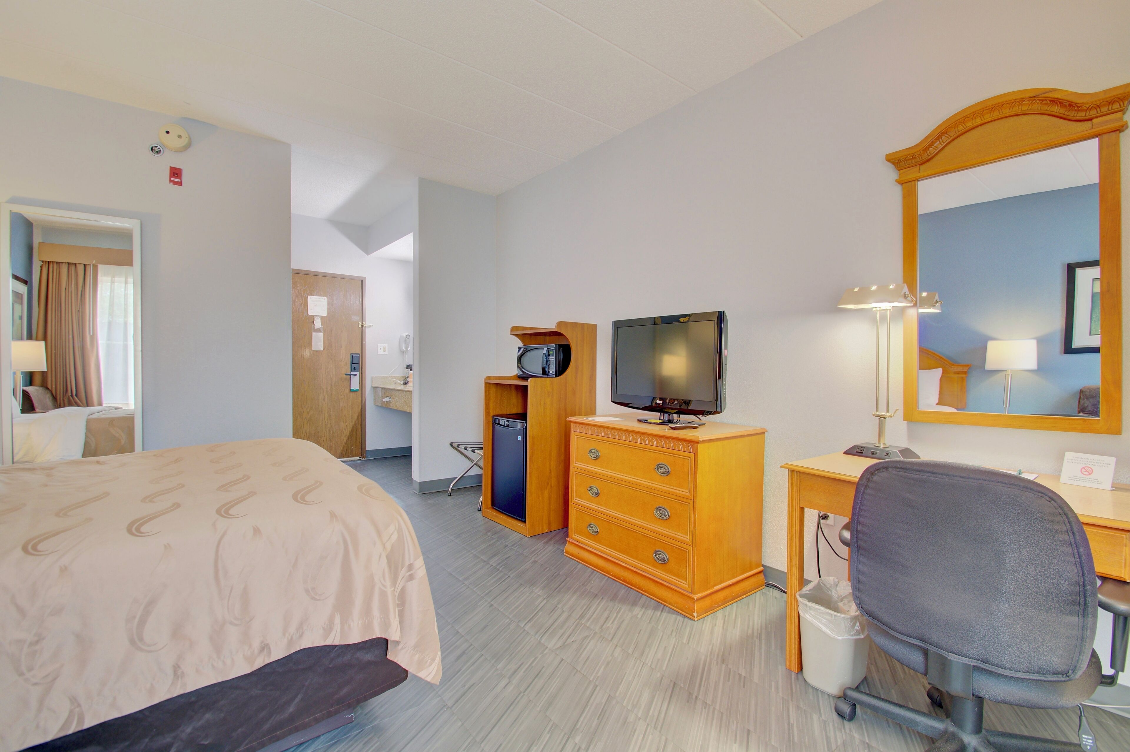 A hotel room with a bed, a desk with a computer, a television, a dresser, and a mirror.