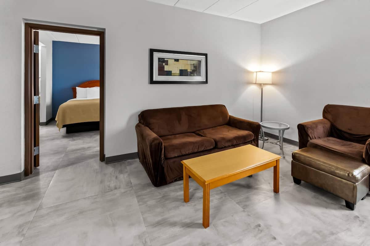 A hotel room with a brown sofa, a wooden coffee table, a small round table, a lamp, and a framed picture on the wall.