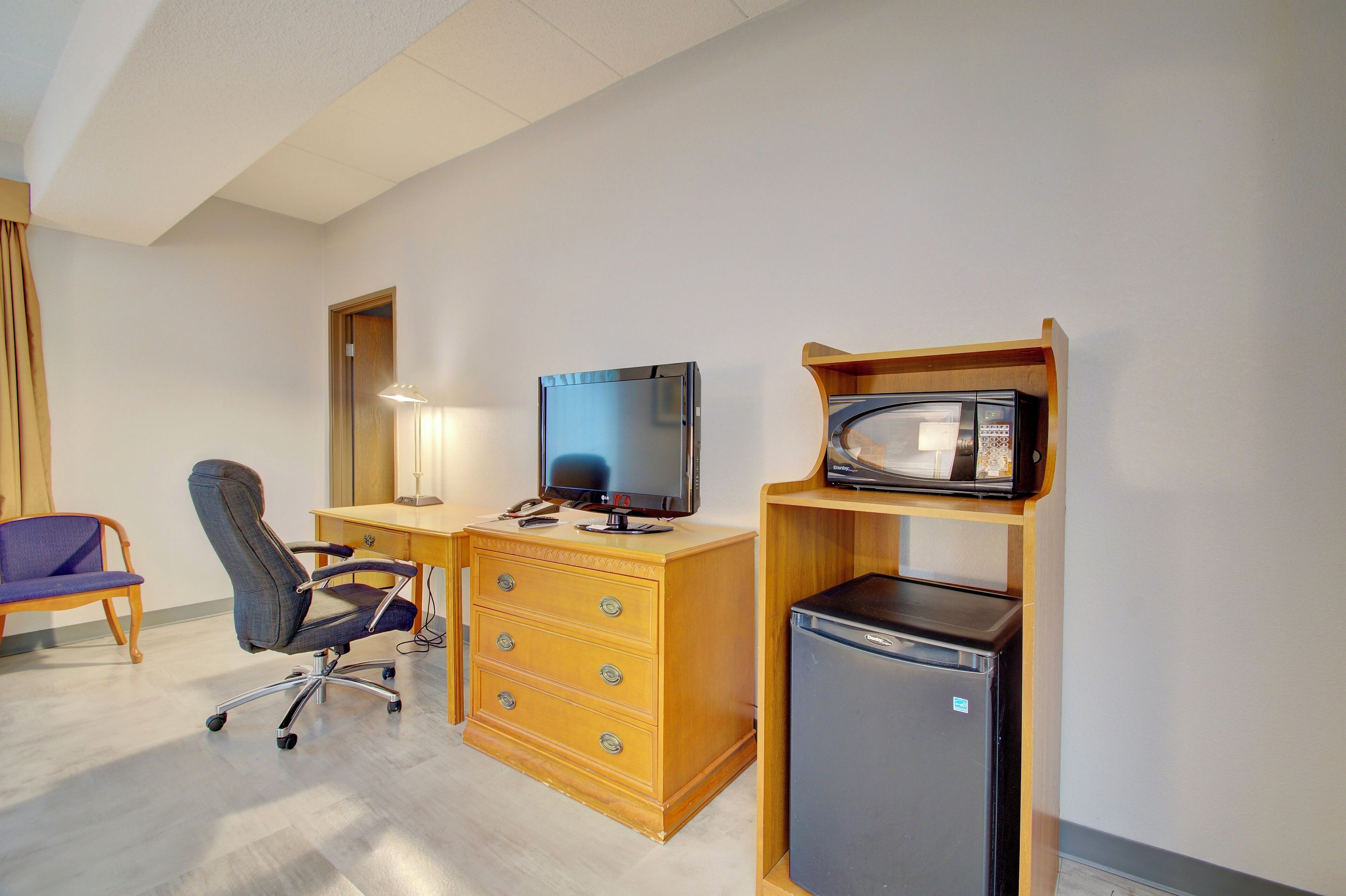 Habitación de hotel con escritorio de madera, televisor, refrigerador, silla y lámpara.
