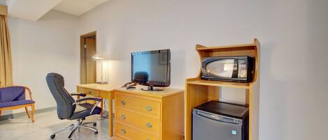 Habitación de hotel con escritorio de madera, televisor, refrigerador, silla y lámpara.
