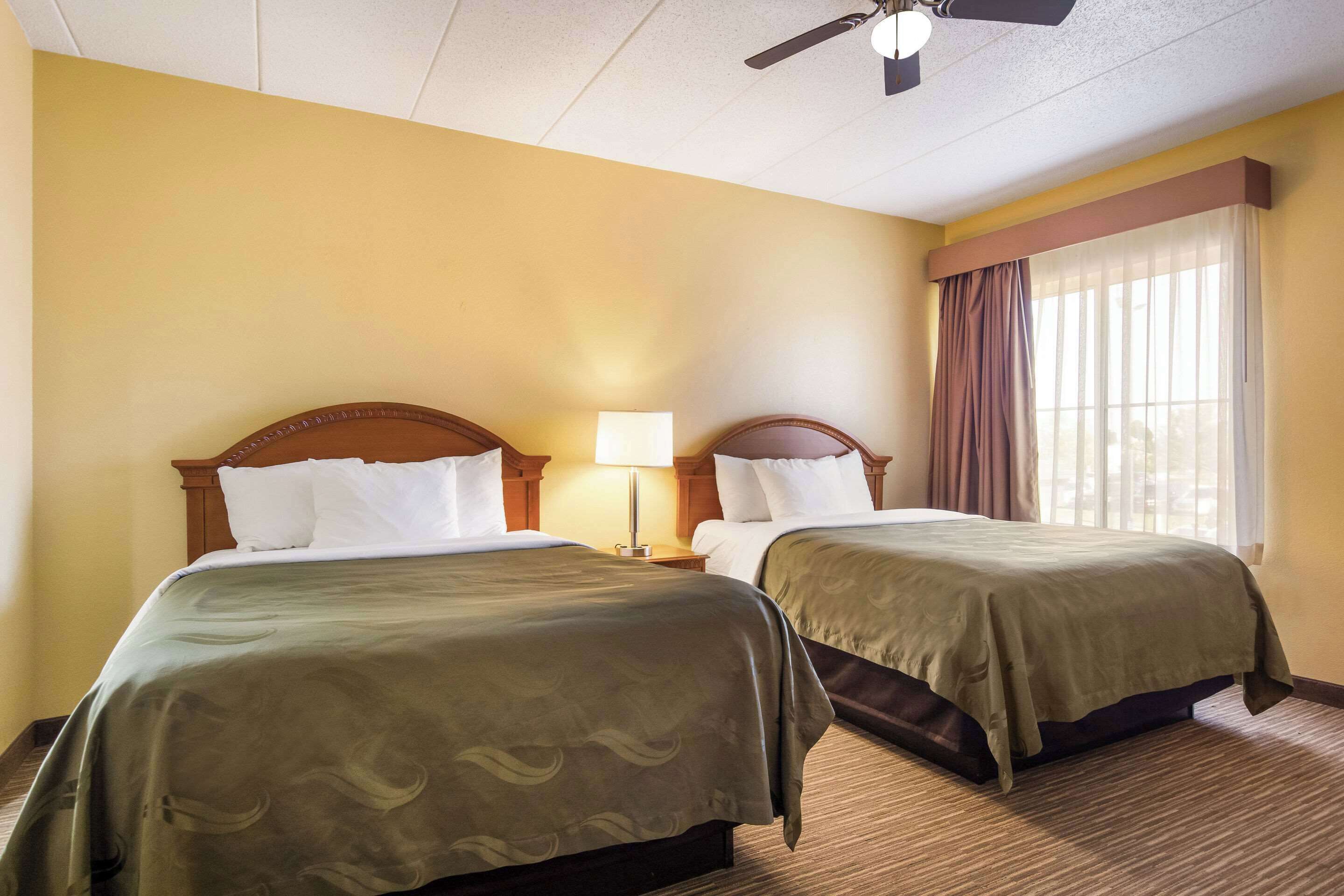 A hotel room with two beds, a ceiling fan, and a window with curtains.
