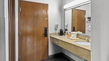Un baño con puerta de madera, lavamanos, espejo, secador de pelo y cafetera.