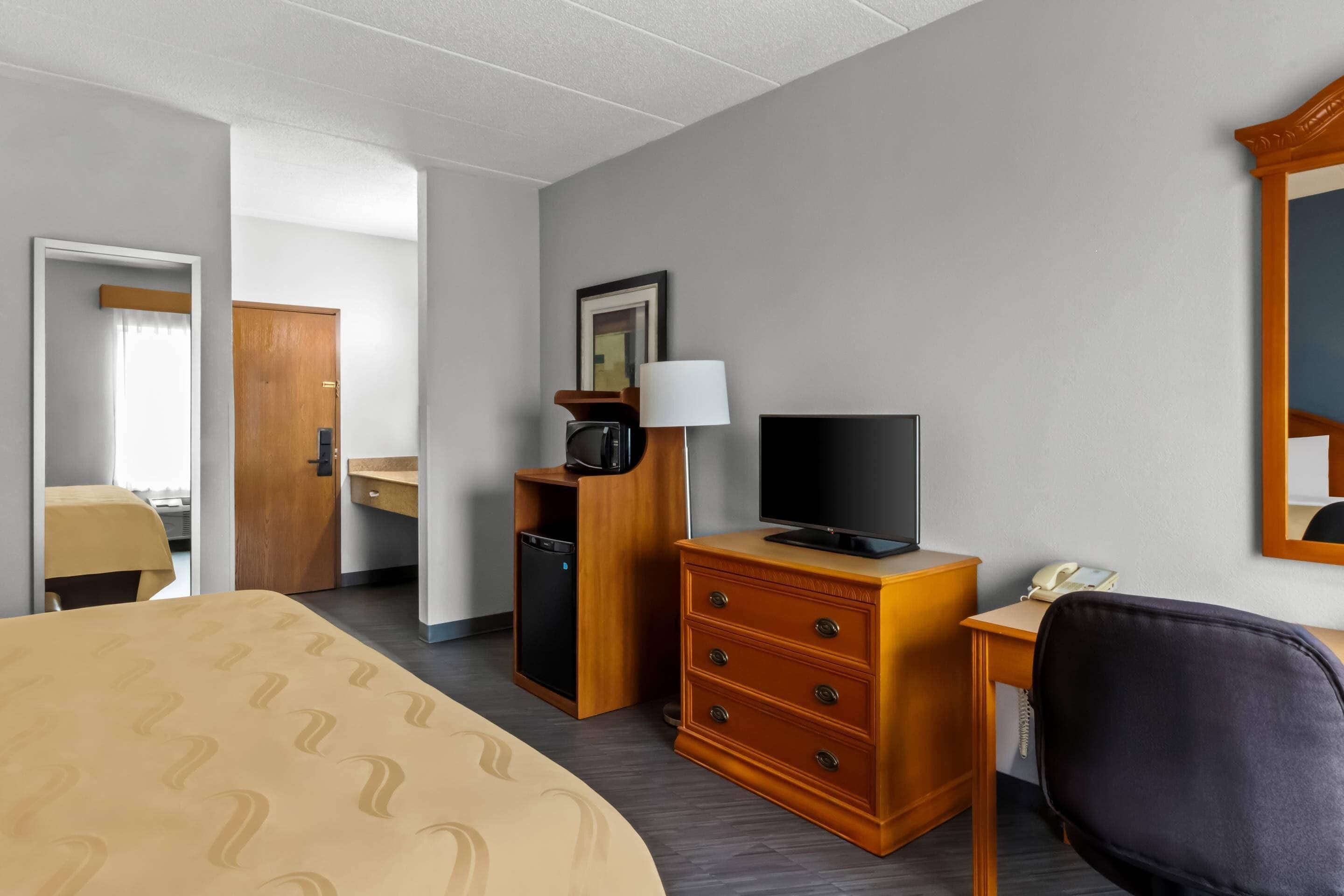 Une chambre d’hôtel équipée d’un lit, d’un bureau avec un téléphone, d’une télévision, d’un four à micro-ondes et d’une commode.