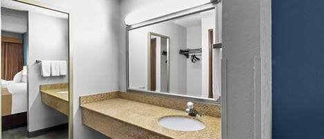 A hotel bathroom with a granite countertop sink, a large mirror, and a visible shower area.