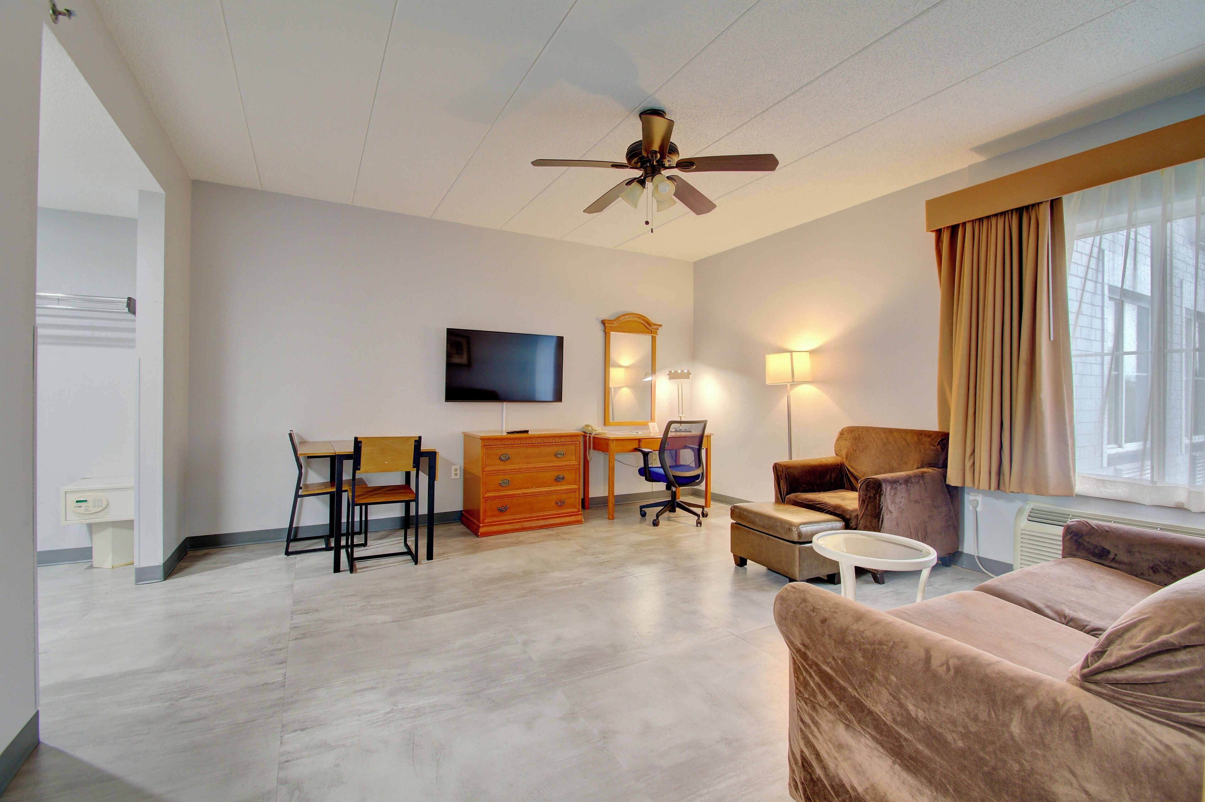 A modern living room with a ceiling fan, a flat-screen TV, a wooden desk, a chair, a sofa, and a small table.