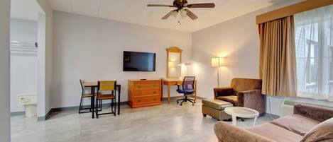 A modern living room with a ceiling fan, a flat-screen TV, a wooden desk, a chair, a sofa, and a small table.