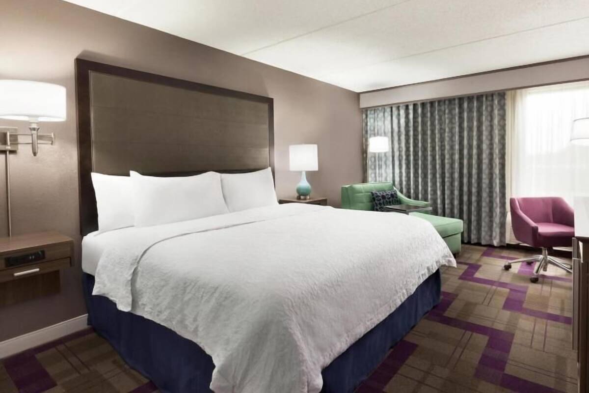 A hotel room with a large bed, a desk, a chair, and a window with curtains.