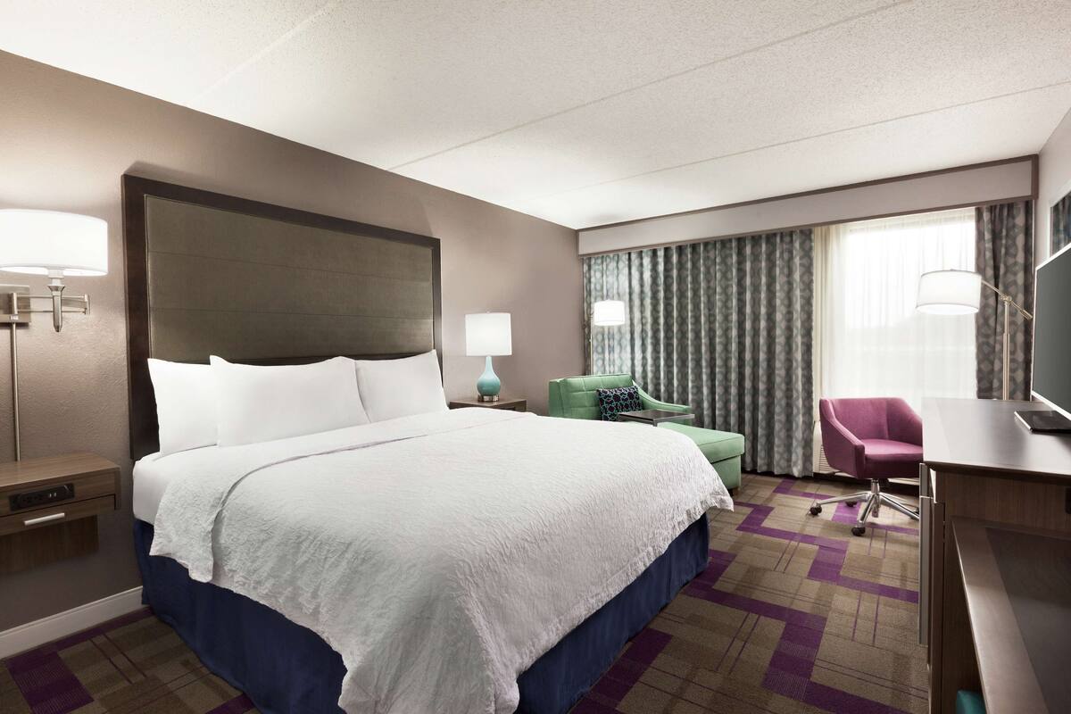 A hotel room with a large bed, a desk, a chair, and a TV.