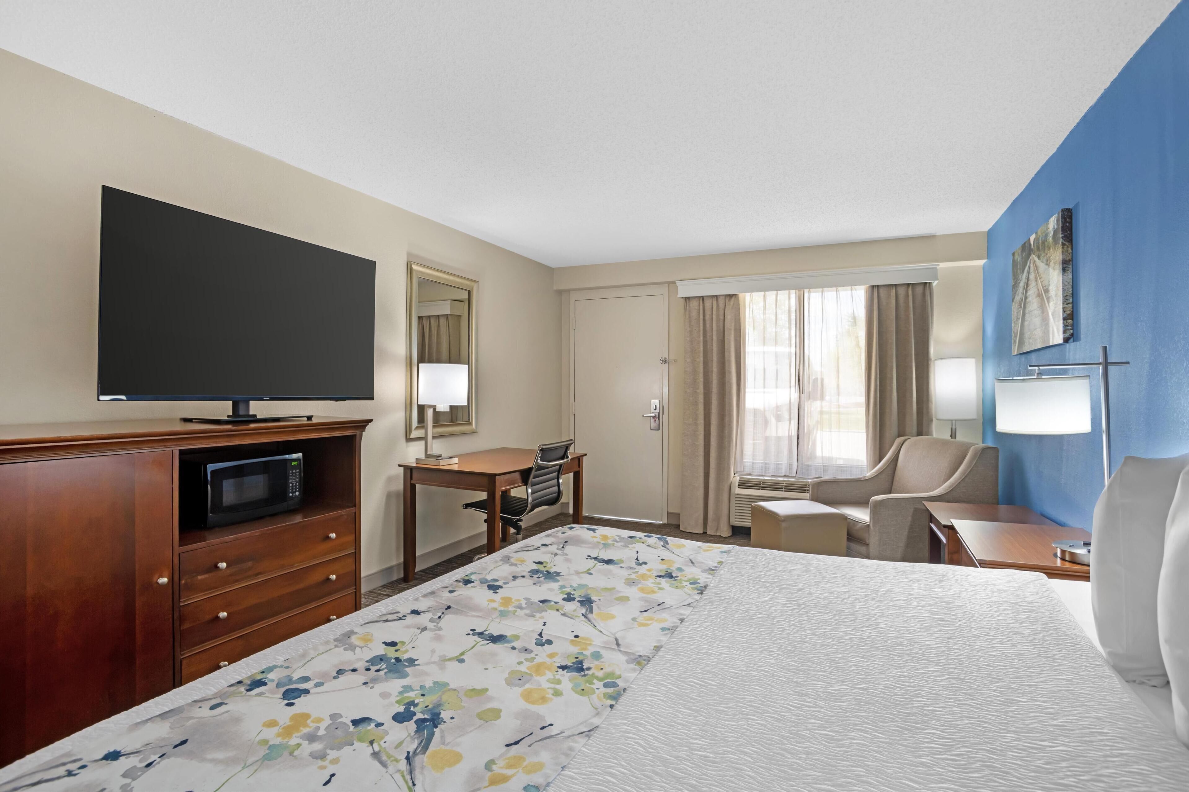 Habitación de hotel con una cama grande, un escritorio con silla, televisor, microondas y ventana con cortinas.