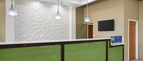 Zona de recepción con una decoración en verde y blanco, un televisor de pantalla plana en la pared y un mostrador de recepción.