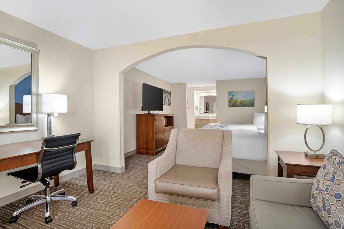 A hotel room with a desk, office chair, two armchairs, a bed, a TV, and a small table.