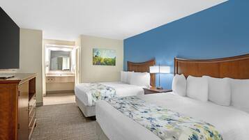 A hotel room with two beds, a desk, a mirror, and a painting on the wall.