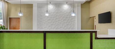 A reception area with a green counter, a textured wall, and a mounted TV.