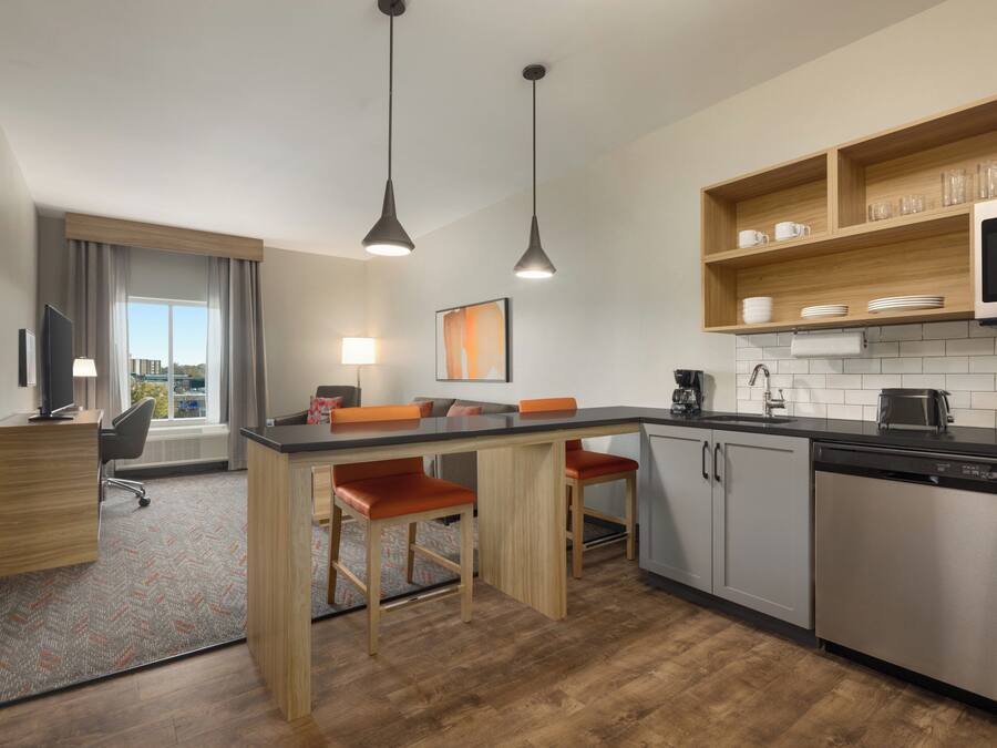 A modern kitchen with a central island, bar stools, a microwave, and a dishwasher.
