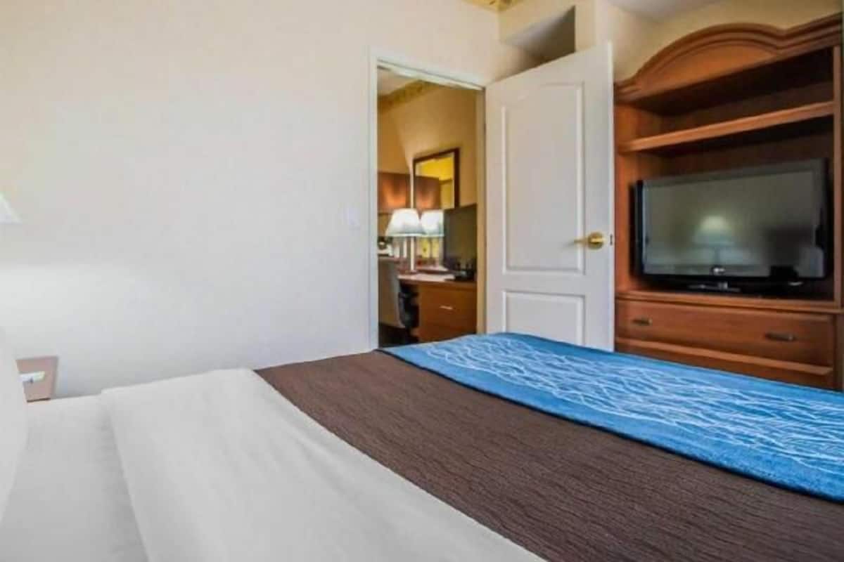 A hotel room with a bed, a television, a wardrobe, and a door leading to another room.