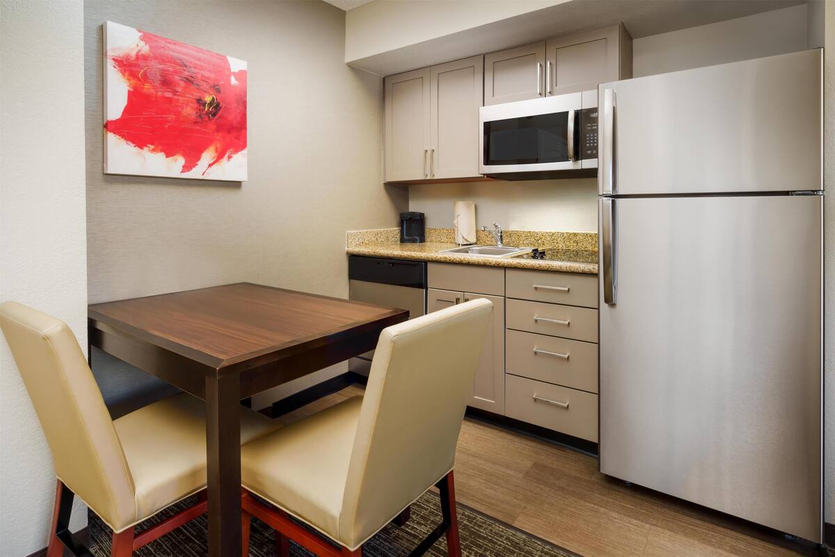 A compact kitchen with a microwave, refrigerator, and a dining table with chairs.