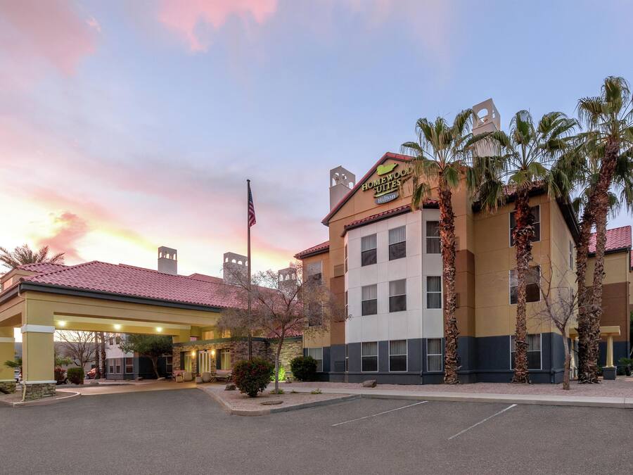 Un hotel con estacionamiento techado, palmeras y un cielo al atardecer.