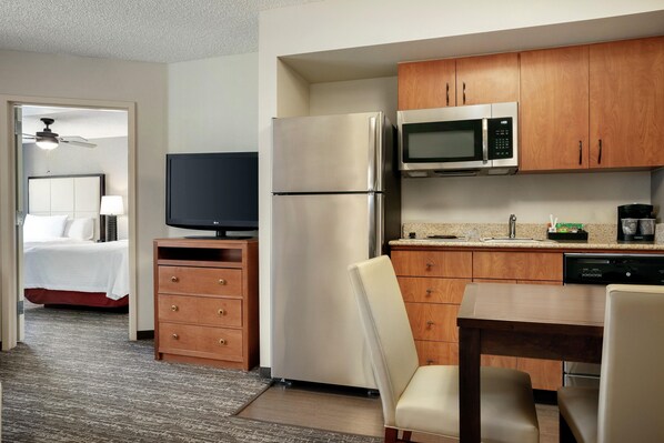 A hotel room with a bed, a television, a refrigerator, a microwave, a wooden cabinet, and a dining area with a table and chairs. - Homewood Suites by Hilton Phoenix/Chandler (Chandler)