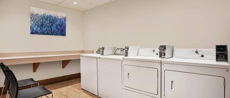 A laundry facility with stacked washers and dryers, a bench, and a wall-mounted artwork.