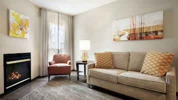 A living room with a fireplace, a sofa, a chair, and two wall-mounted artworks.