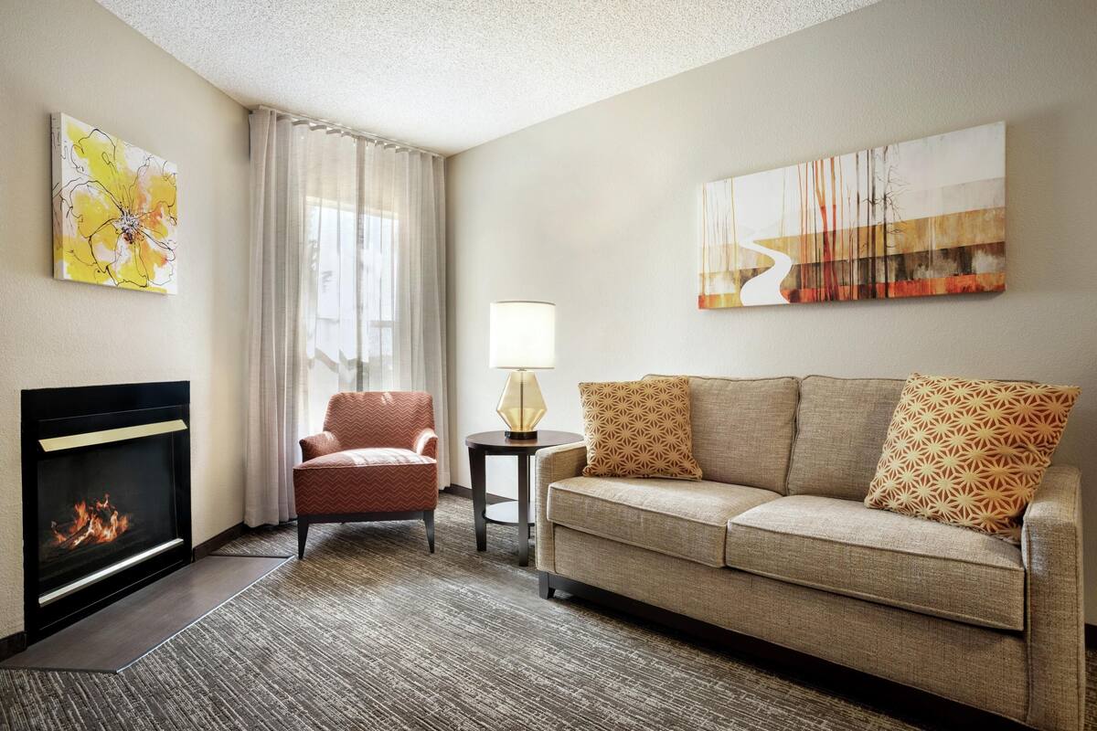 A living room with a fireplace, a sofa, a chair, and two wall-mounted artworks.