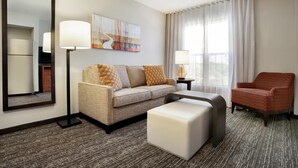 Habitación de hotel con sofá, reposapiés, sillón, lámpara y obra de arte en la pared.