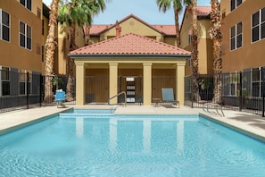 A swimming pool with a covered area, palm trees, and a building with a red-tiled roof. - Homewood Suites by Hilton Phoenix/Chandler (Chandler)
