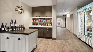 Una cocina de hotel con una isla central, un colgante de luz y un refrigerador lleno de bebidas.