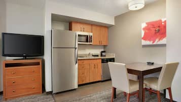 A compact kitchen with a refrigerator, microwave, and wooden cabinets. There is a dining table with chairs and a television on a stand.