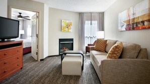 Una habitación de hotel con televisión, sofá, chimenea y obras de arte en las paredes.