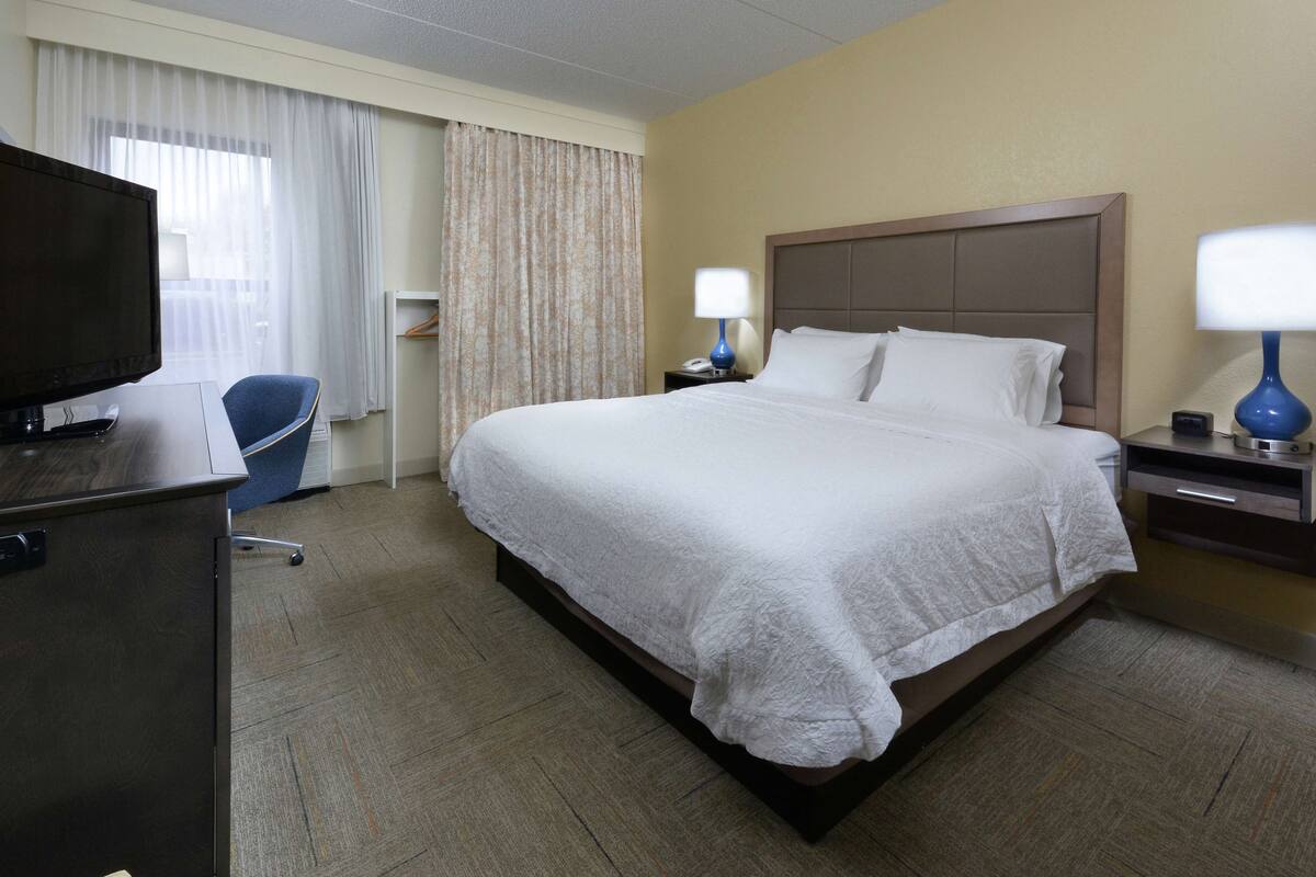 A hotel room with a large bed, a desk with a television, two bedside lamps, and a chair.