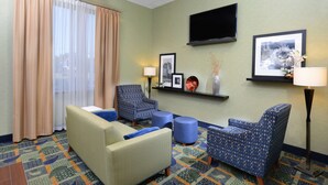 A hotel room with a sofa, two patterned armchairs, a coffee table, a TV mounted on the wall, and a patterned carpet. - Hampton Inn High Point (High Point)