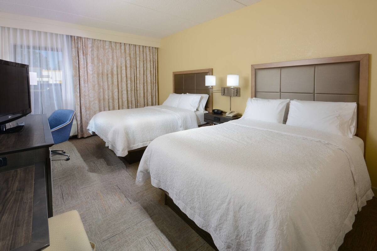 A hotel room with two beds, a desk with a television, and a chair.