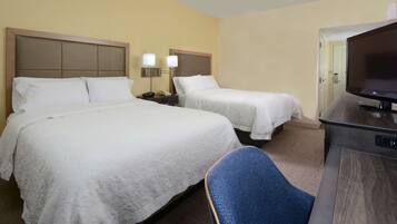 A hotel room with two beds, a desk with a flat-screen TV, and a blue chair.