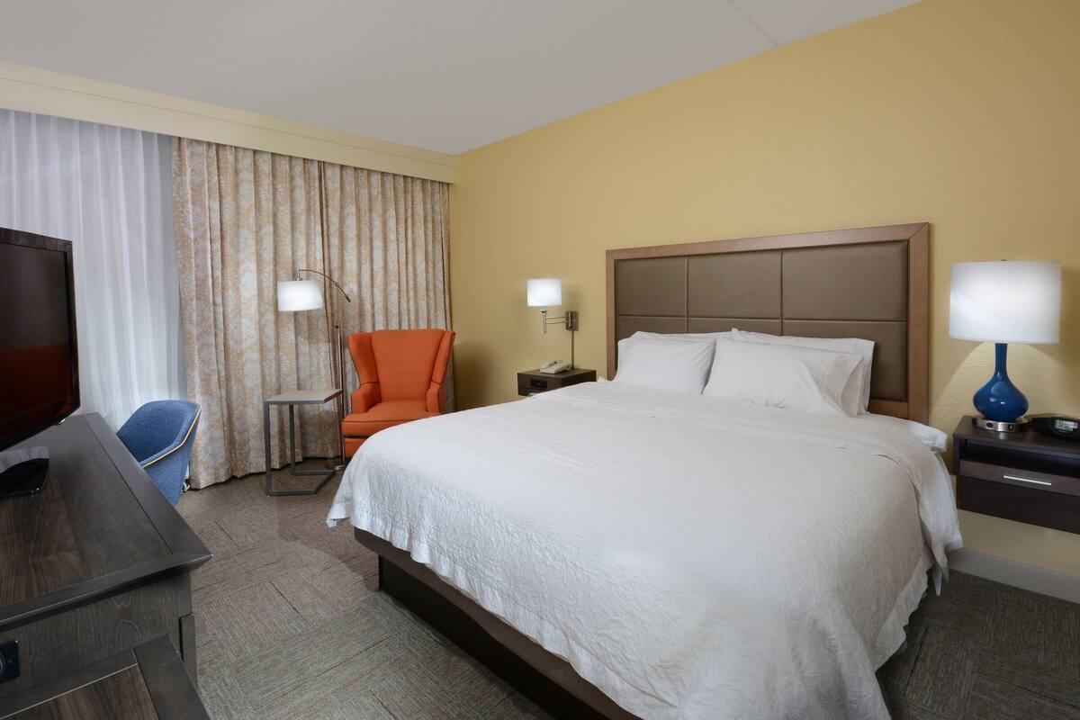 A hotel room with a large bed, a desk, a chair, and two bedside lamps.