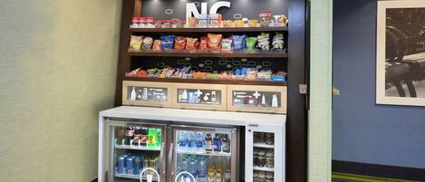 Una exhibición de botanas con papas fritas y otros refrigerios, un refrigerador para bebidas y un letrero sobre las botanas.