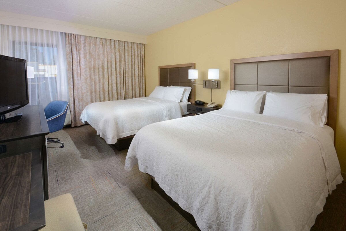 A hotel room with two beds, a TV, a desk, and a chair.