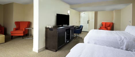 A hotel room with two beds, a desk with a television, and two red chairs.