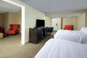A hotel room with two beds, a desk with a television, and two red chairs.