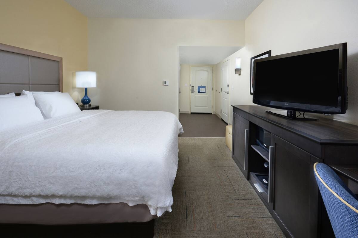 A hotel room with a bed, a TV on a dresser, and a door leading to another room.