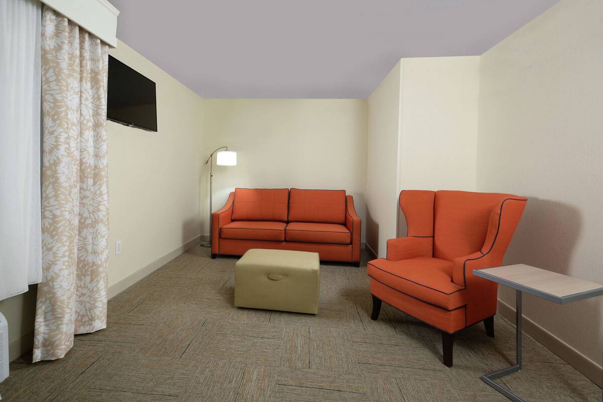 A room with a beige ottoman, an orange armchair, and a sofa.