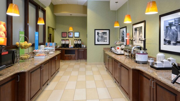 A hotel kitchen with granite countertops, wooden cabinets, and overhead pendant lighting. - Hampton Inn High Point (High Point)