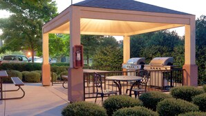 A covered outdoor patio with a grill, seating, and a power outlet. - Sonesta Simply Suites Jacksonville (Jacksonville)