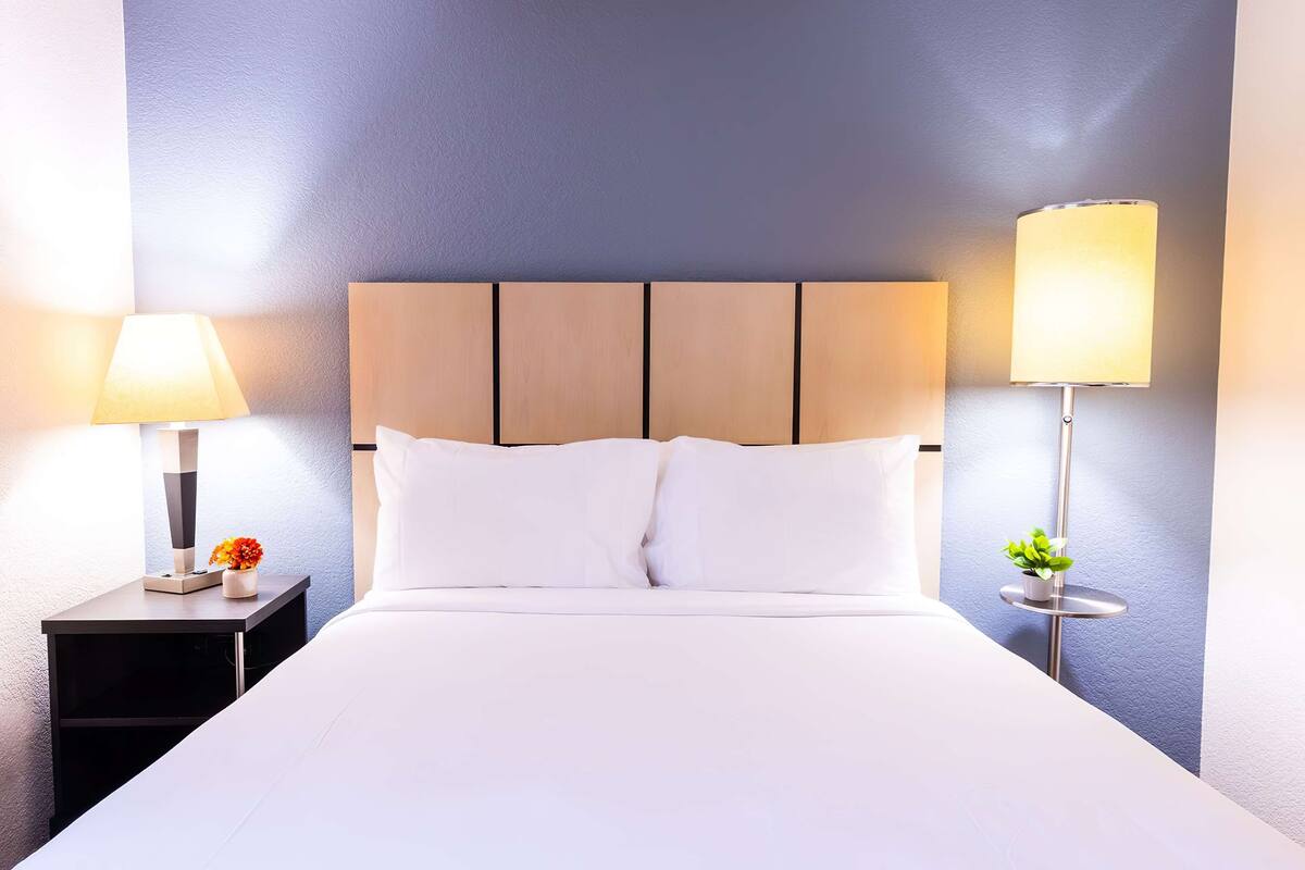 A neatly made bed with white linens, a wooden headboard, and two bedside lamps.