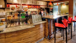 A restaurant with a wooden counter, menu boards, and red chairs. - Courtyard by Marriott Burlington (Burlington)