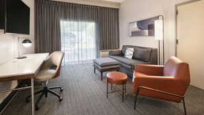 A hotel room with a desk, office chair, sofa, ottoman, and a single armchair. - Courtyard by Marriott Burlington (Burlington)