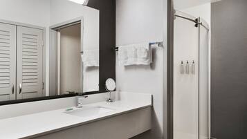 A modern bathroom with a white sink, a large mirror, a round mirror, and a glass-enclosed shower.