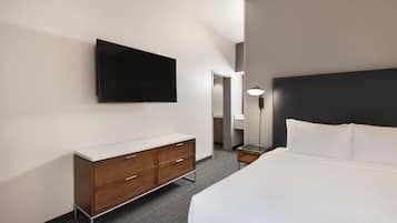 Een hotelkamer met een bed, een flatscreen televisie aan de muur, een houten dressoir en een nachtkastje met een lamp.