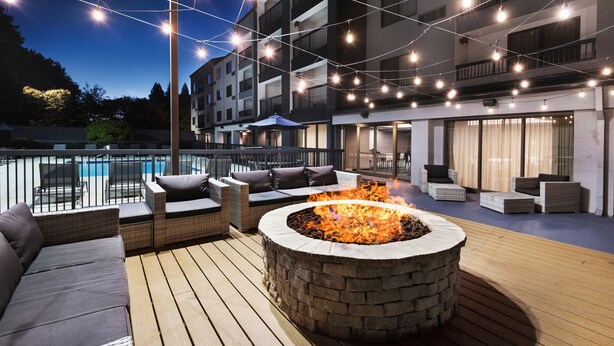 An outdoor deck with a stone fire pit, seating area, and string lights. - Courtyard by Marriott Burlington (Burlington)